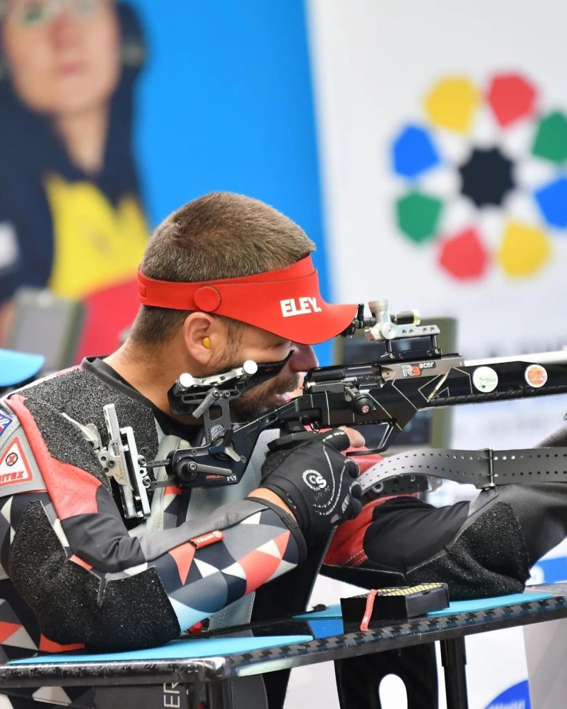 A side view of Matt Skelhon shooting for Gold at Grenada 2024 with the targets in the background